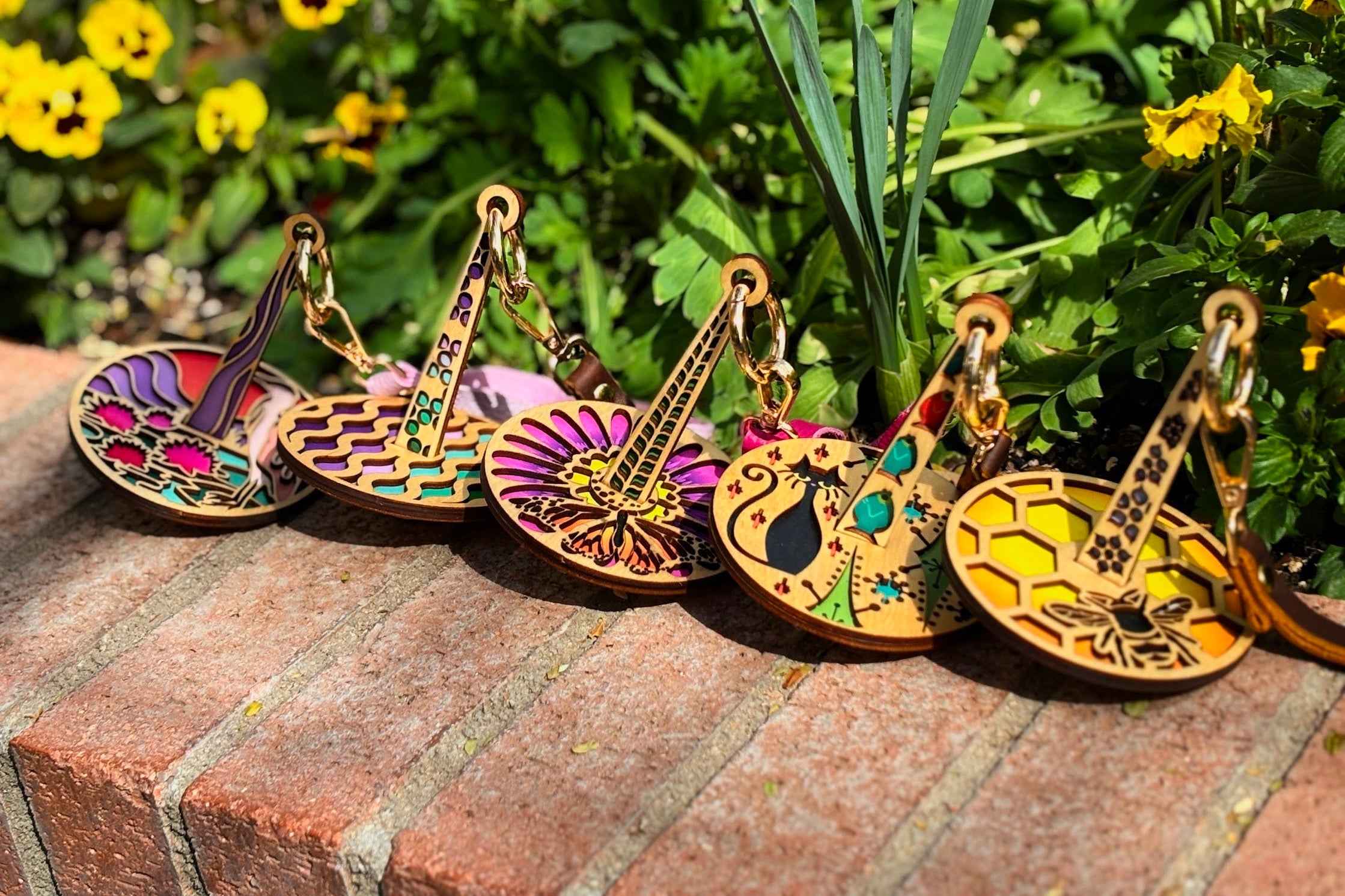 Colorful wrist yarn holders on a brick surface with greenery and flowers in the background