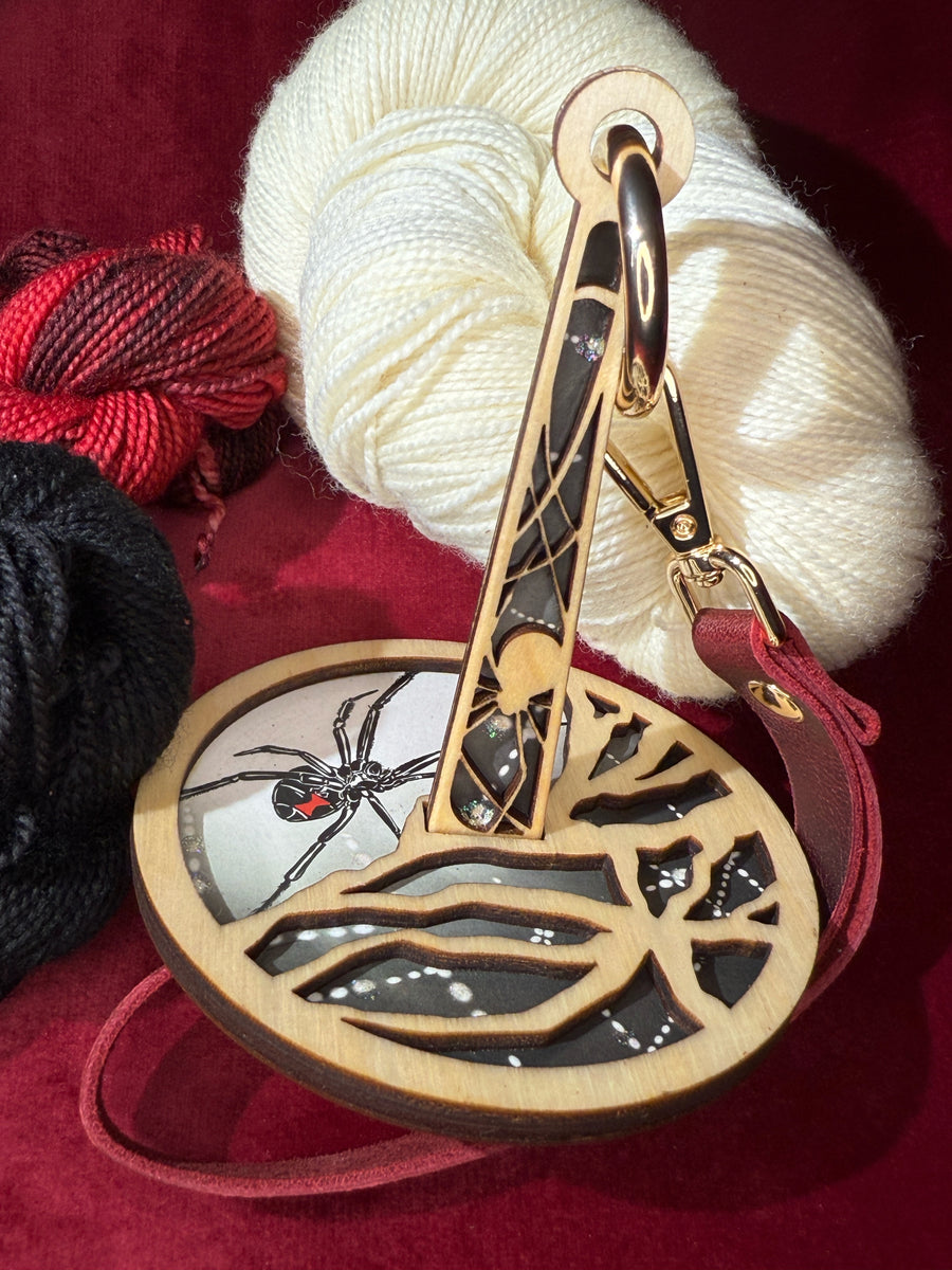 Decorative wrist yarn holder with a black widow design on a red fabric background