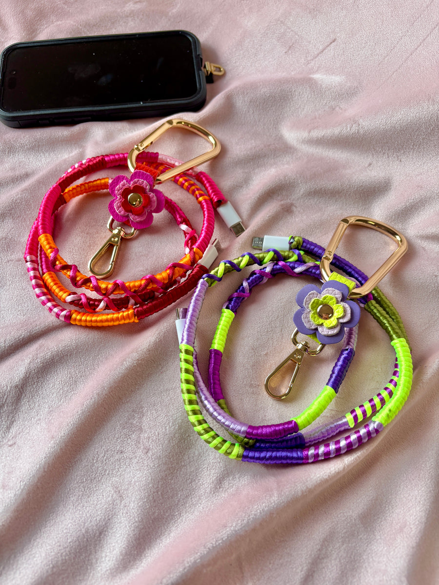 Two colorful phone charging cables with floral phone clips on a light pink fabric background.