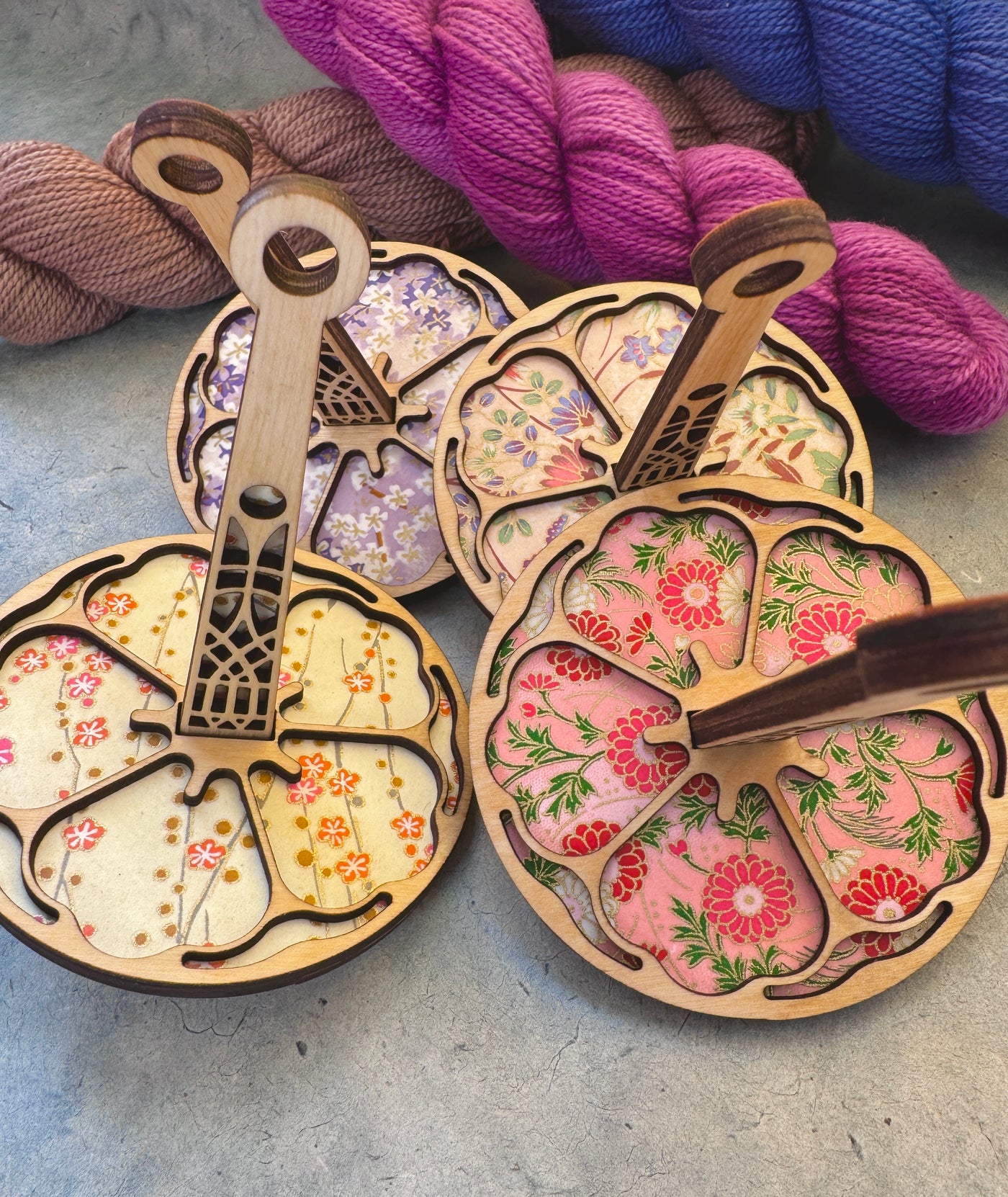 Wooden wrist yarn holders with floral patterns on a textured gray surface with yarn in the background.