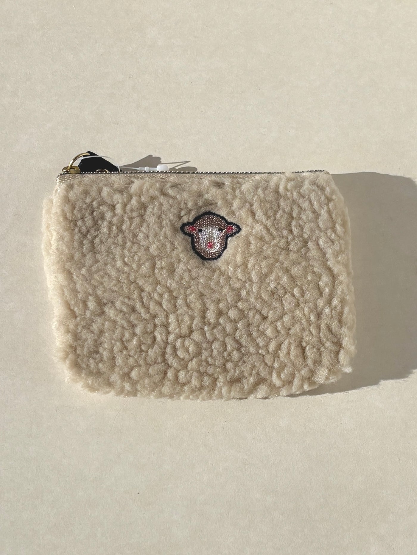 Beige sherpa pouch with a logo on a light gray background
