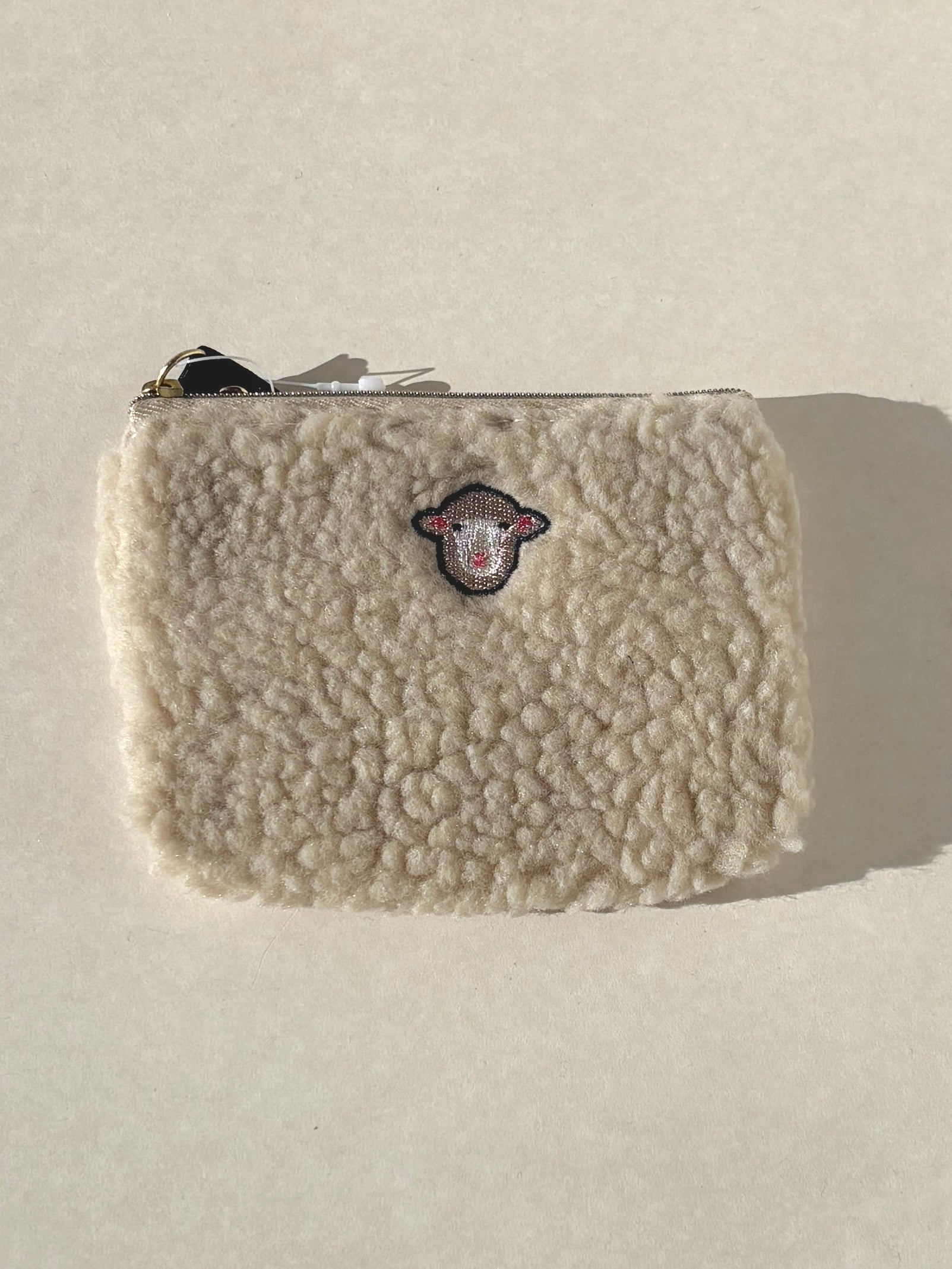 Beige sherpa pouch with a logo on a light gray background