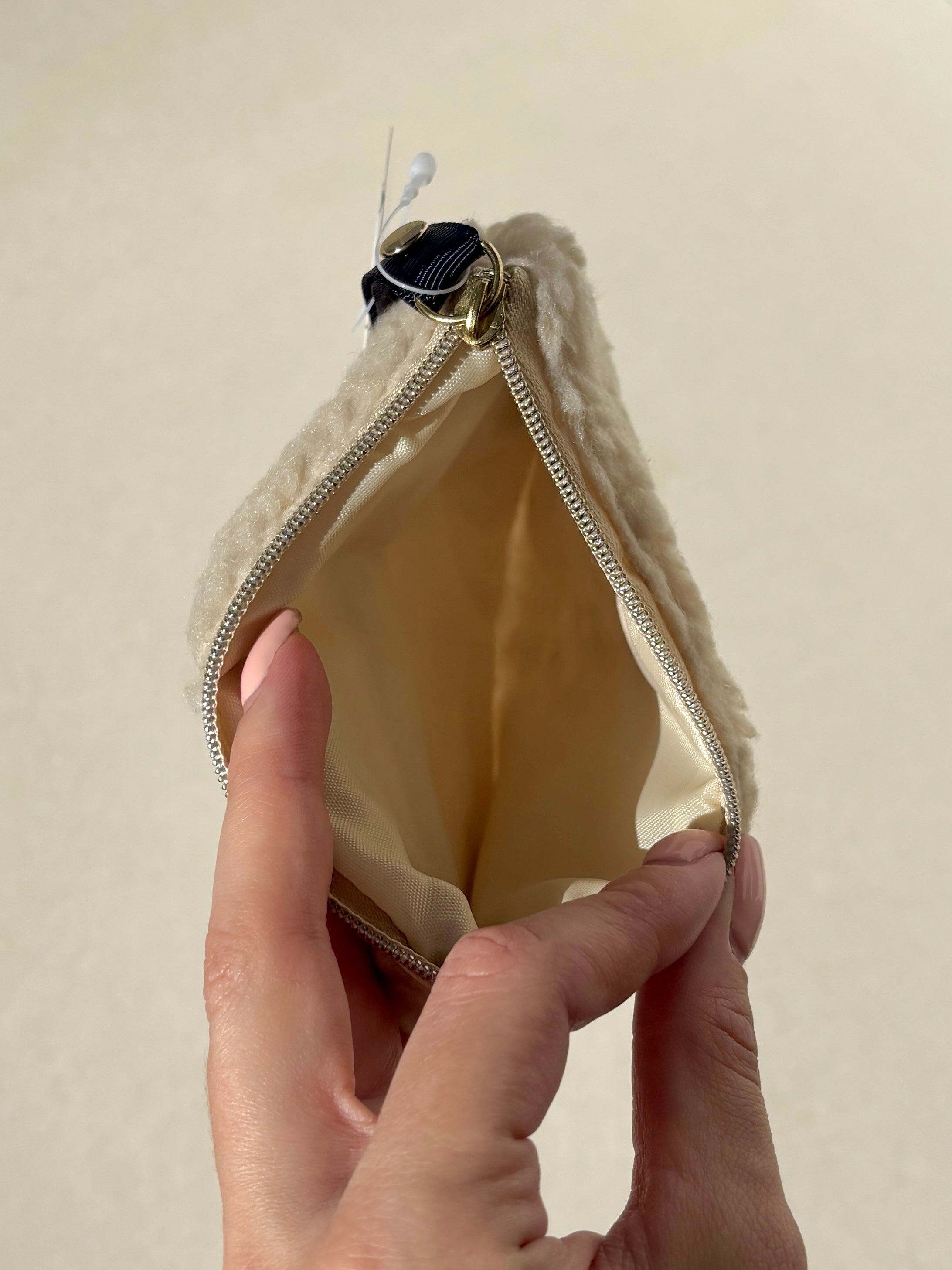 Hand holding an open beige accessory pouch with a zipper against a beige background