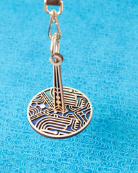 A decorative circular yarn holder with a geometric pattern, attached to a leather wrist strap, for knitting or crochet enthusiasts.