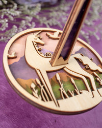 A closeup of a yarn ball holder with a unicorn pattern, displayed on a purple background.