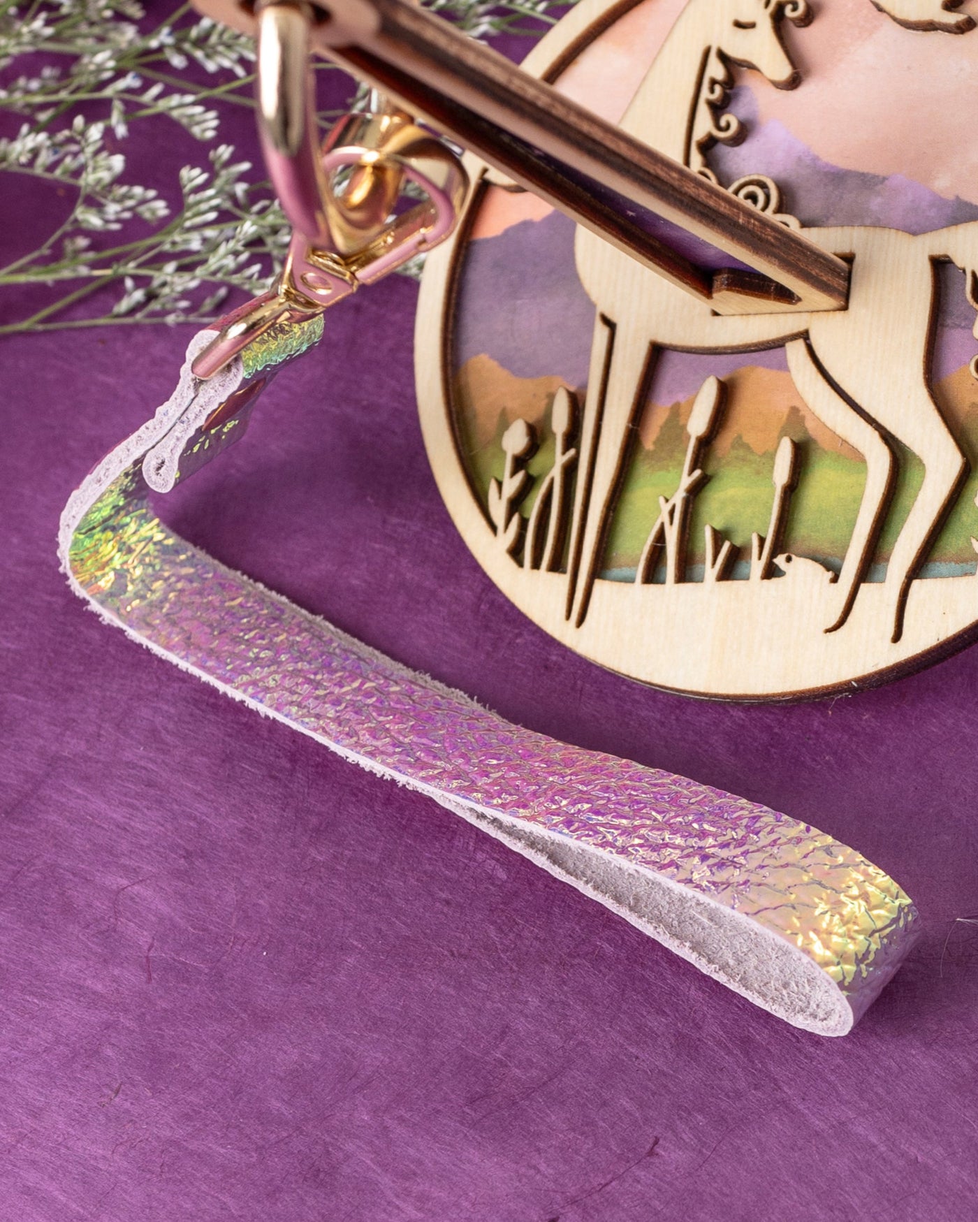 A close up of a lavender and yellow iridescent leather, attached to a yarn holder with a unicorn design, displayed on a purple background with yarn balls around it.