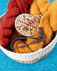 A wooden yarn holder featuring ocean-themed graphics, with an attached dark blue leather strap, sitting on top of a basket full of yarn.
