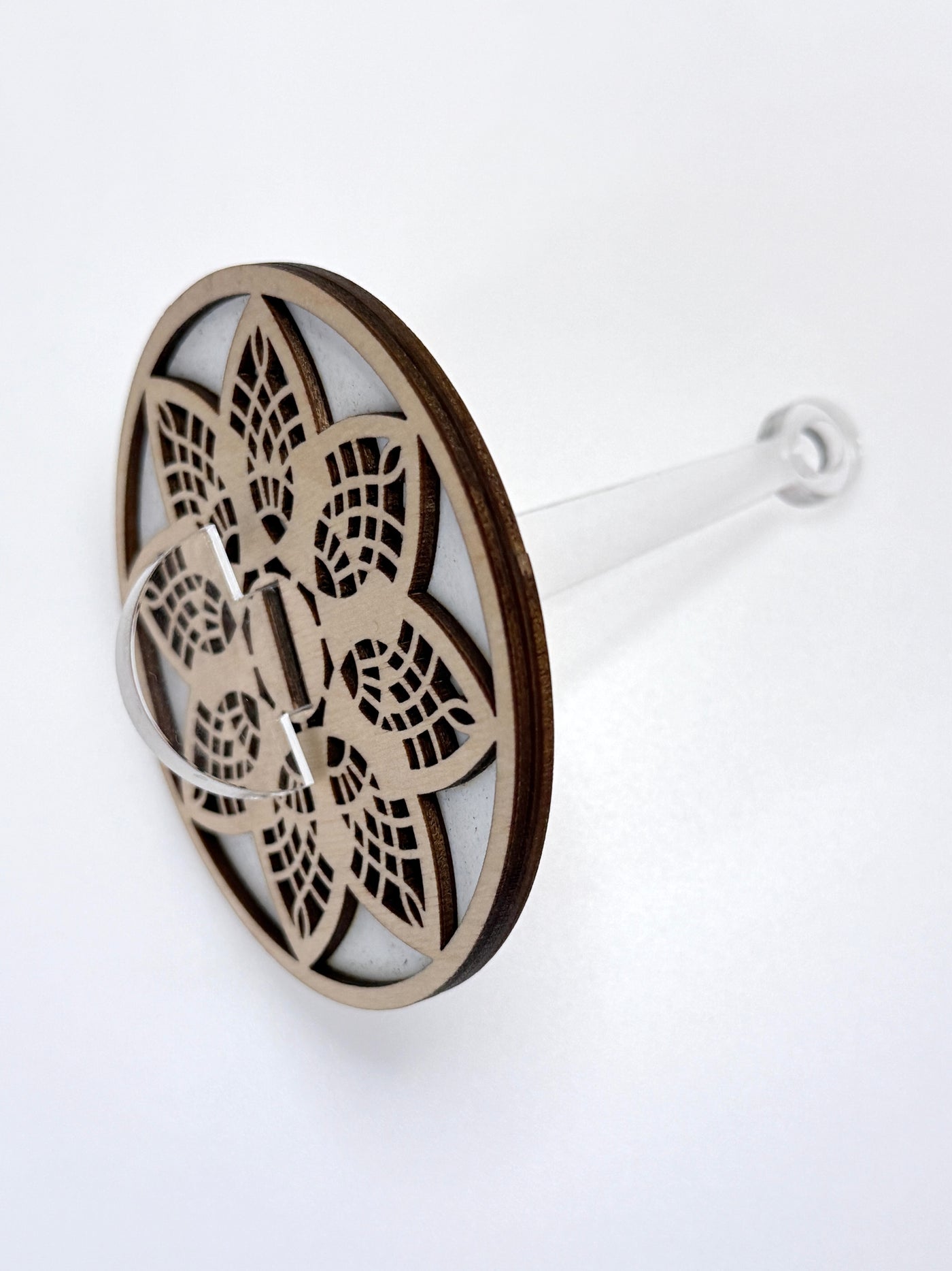 Decorative wooden yarn holder plate with intricate cut-out design and a clear stick on a white background
