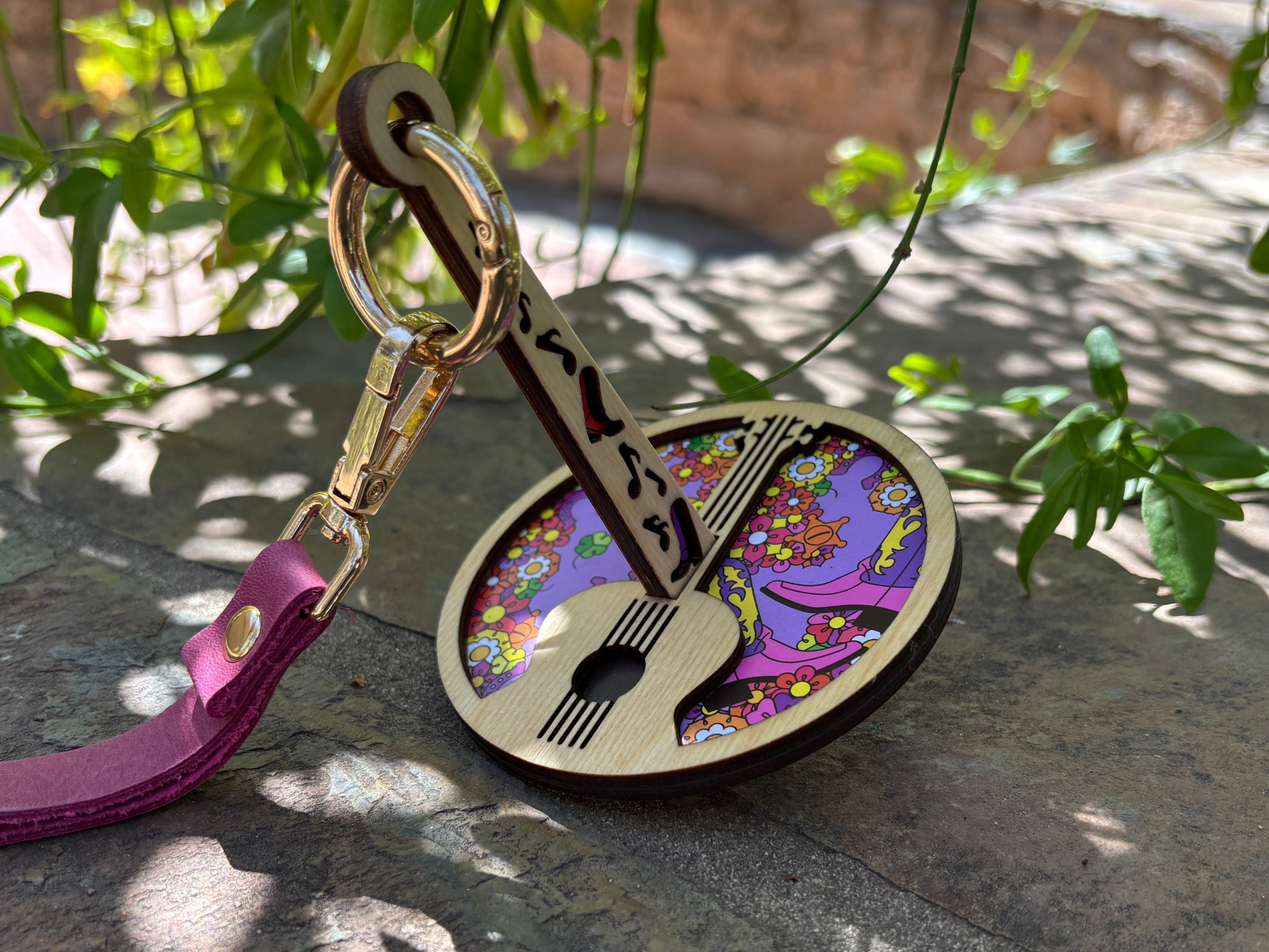 Handcrafted portable yarn holder featuring a floral pattern and guitar motif, displayed on a rock pathed under green foliage.