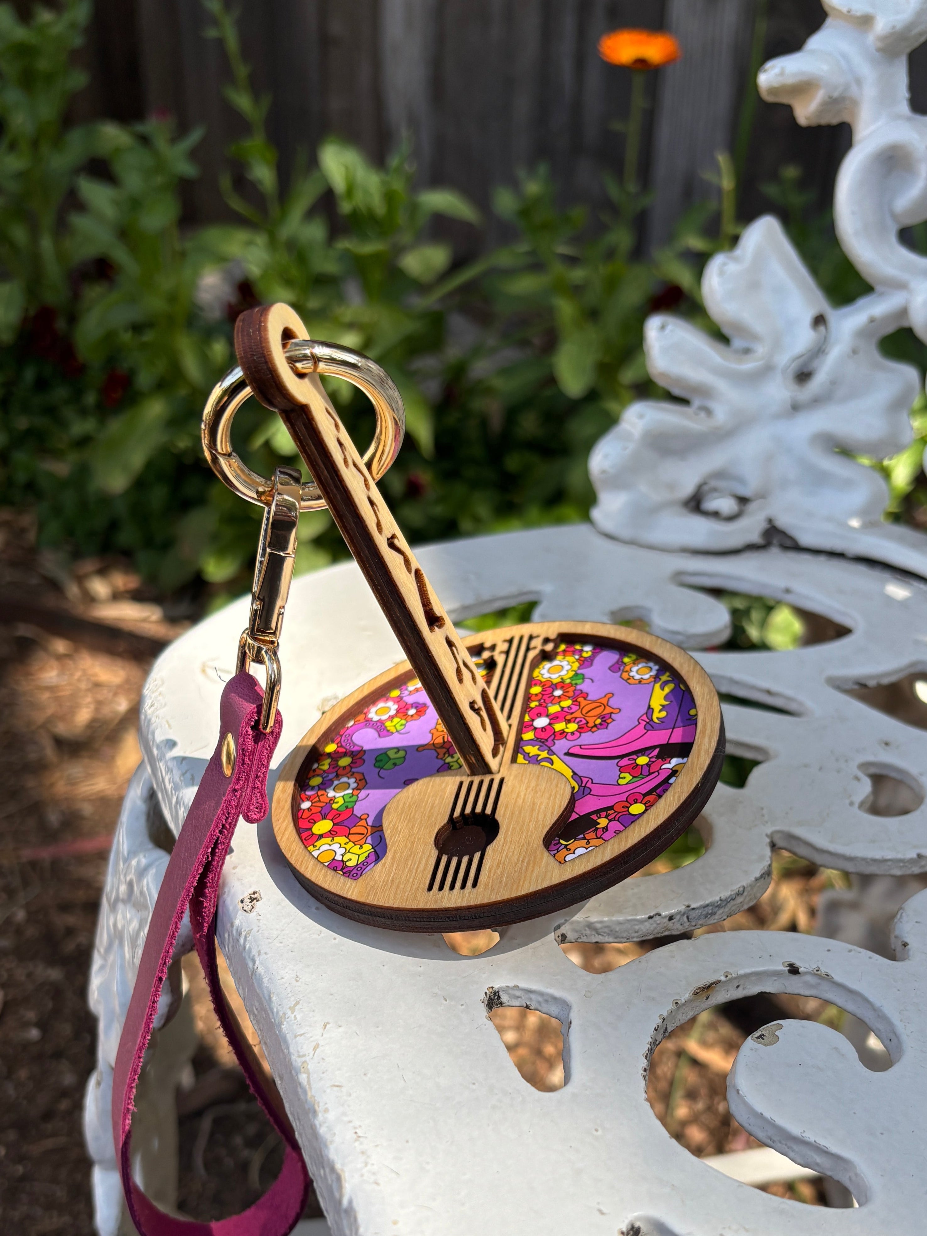 A wrist‑strap yarn holder decorated with bright florals and a guitar graphic, photographed on an ornate white surface, in a garden.