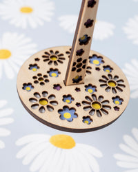 A close up look of a portable yarn holder with a floral pattern, displayed on a fabric with daisy prints.