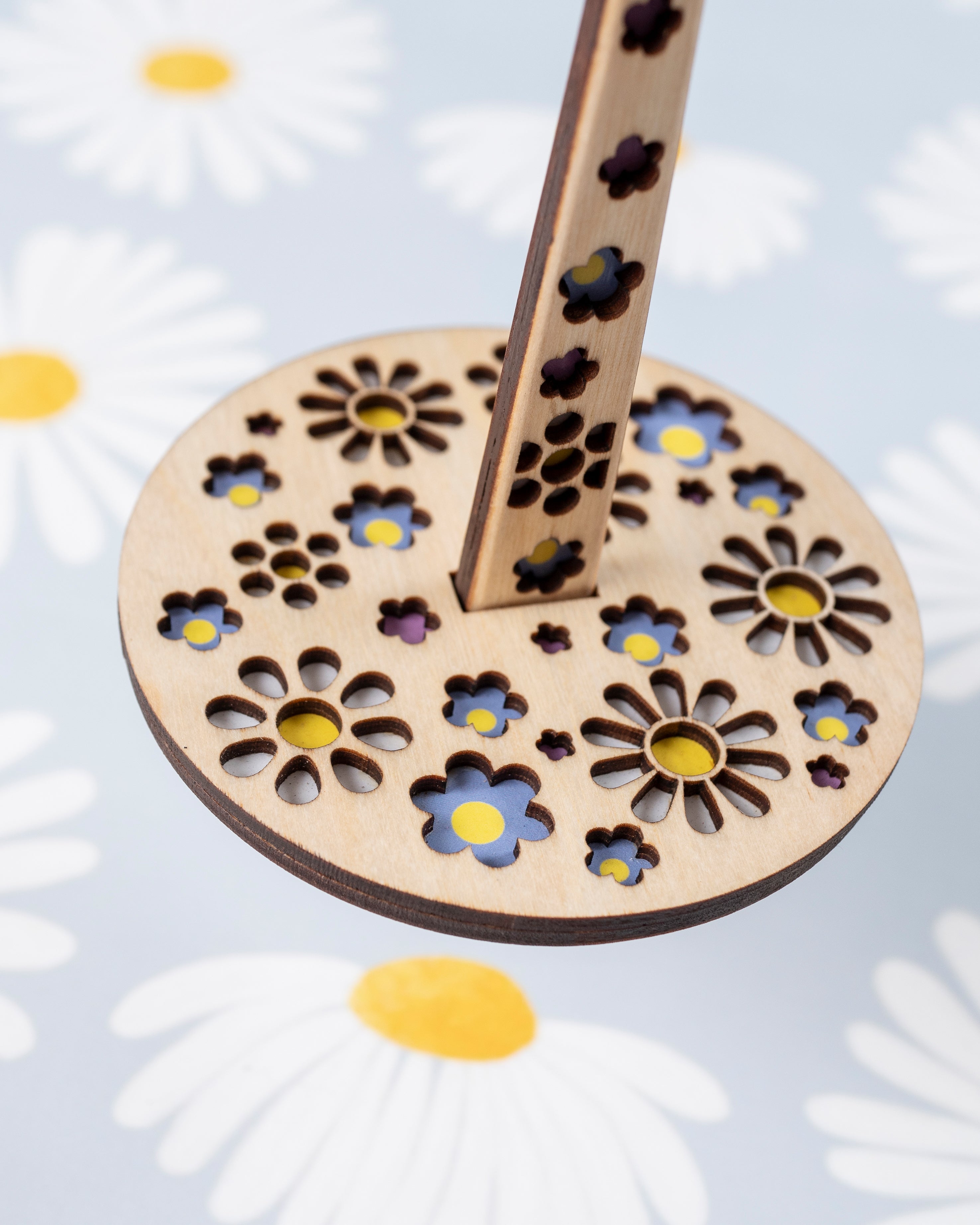 A close up look of a portable yarn holder with a floral pattern, displayed on a fabric with daisy prints.