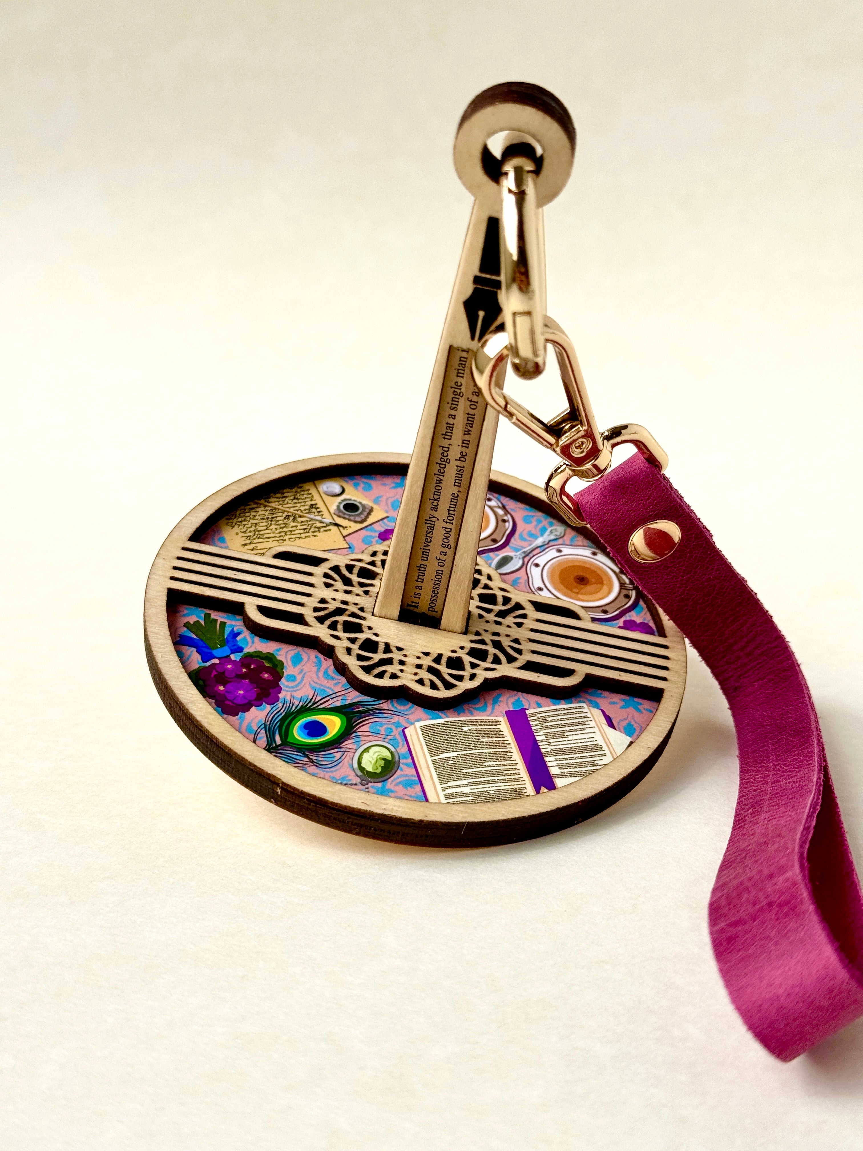 Decorative wrist yarn holder with colorful Pride & Prejudice themed table scape design and pink leather strap on a white background.