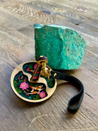 A portable yarn minder decorated with two koi fish swimming among green lily pads and pink lotuses, displayed beside a turquoise rock on a wooden surface.