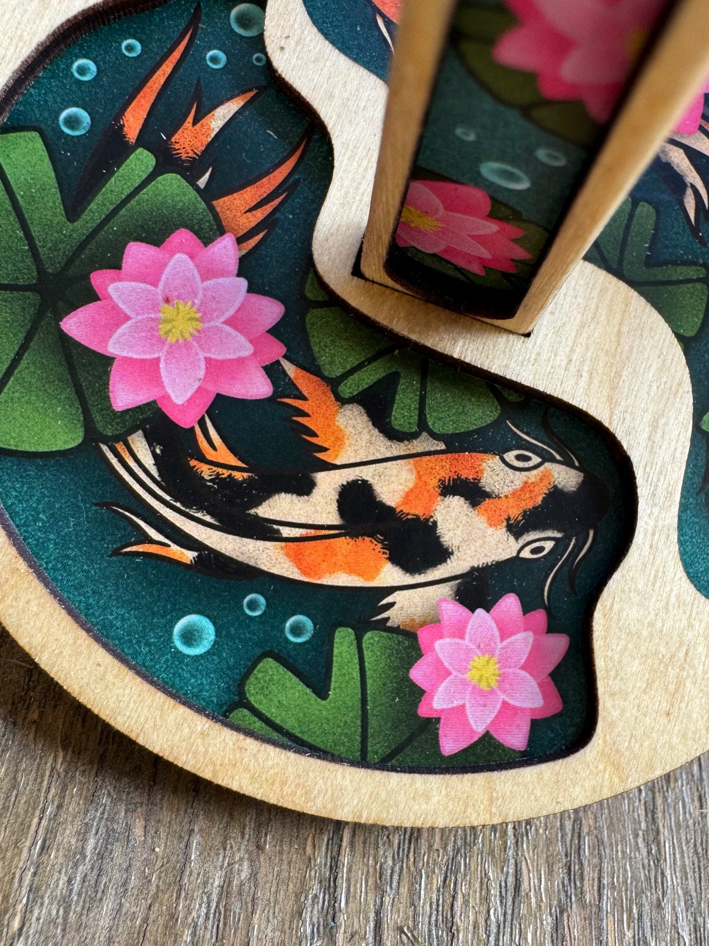 Detail shot of the one of the koi fish on the circular wooden mini minder yarn holder plate.
