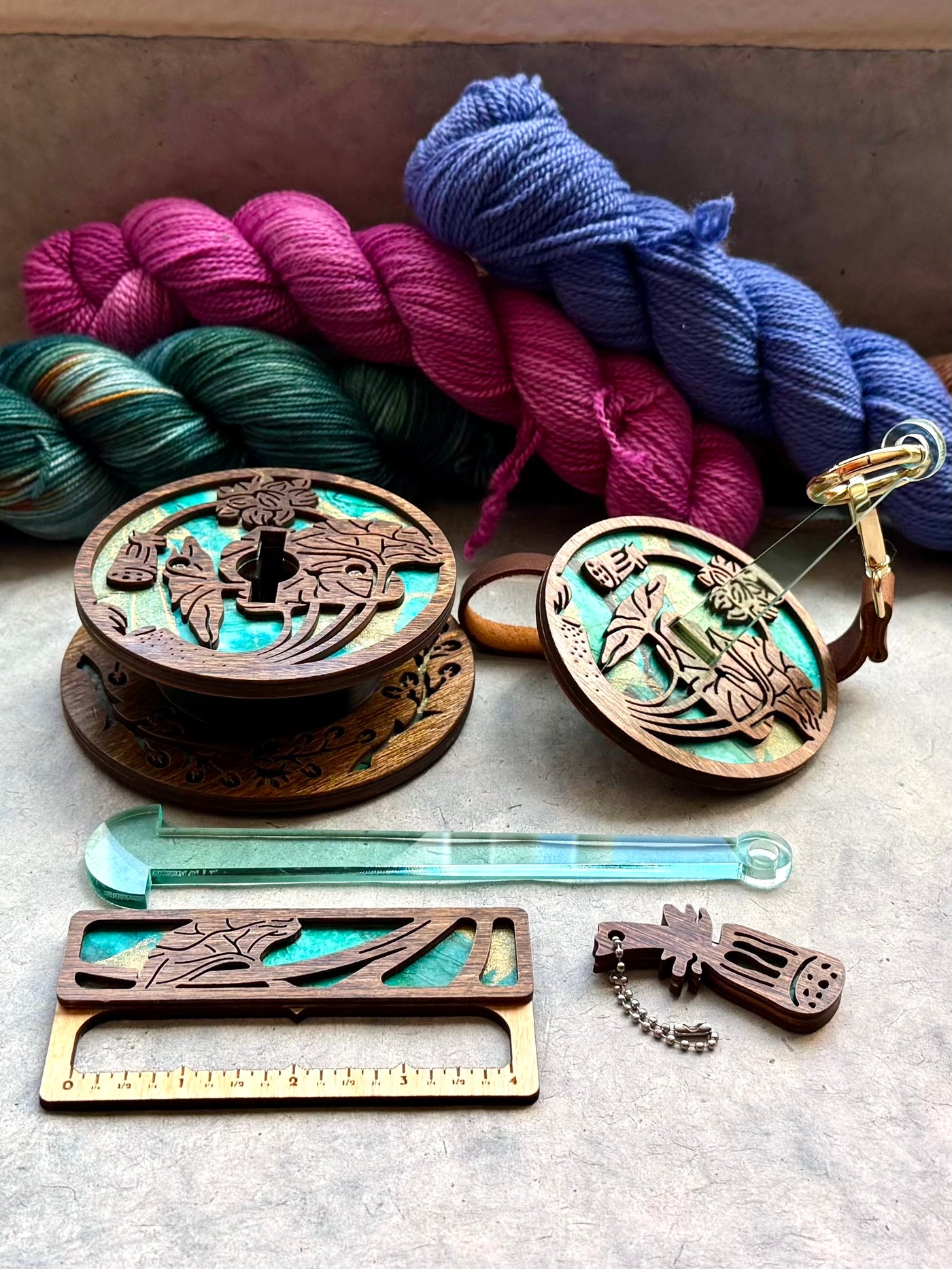 A collection of knitting and crochet tools made from dark wood and turquoise paper, including a portable yarn holder, a swatch gauge, and a yarn cutter.