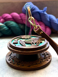 A Lemonwood Mini Minder yarn holder sitting on its tabletop companion the Whirl. Both items are made from a dark-stained wood.
