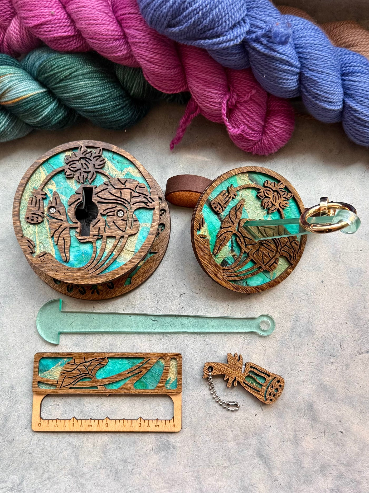 A collection of knitting and crochet tools made from dark wood and turquoise paper, including a portable yarn holder, a swatch gauge, and a yarn cutter.