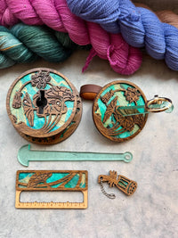 A collection of knitting and crochet tools made from dark wood and turquoise paper, including a portable yarn holder, a swatch gauge, and a yarn cutter.