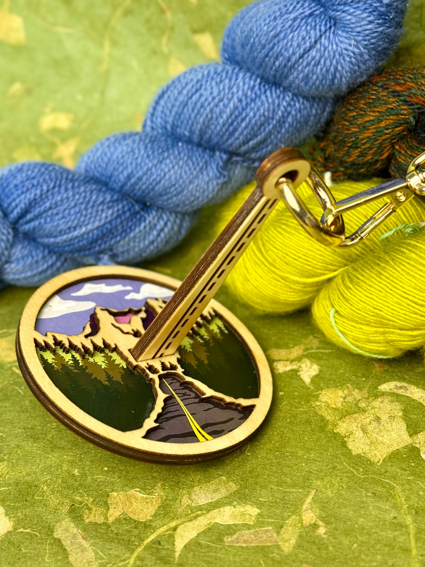 Wood yarn holder with a mountain design positioned on a green backdrop with yarn placed around it.